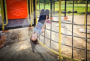Asian girl is hanging upside down on a playground outdoor and looking at camera in the park,summer,vacation concept