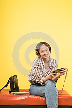 asian girl with headphones using smartphone while sitting with books and bag