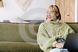 Asian girl laughing and working with laptop while resting on sofa