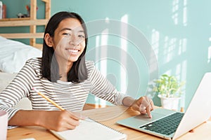 Asian girl learning online via the internet tutor on a laptop computer, Asia child is studying while sitting Interior at home photo