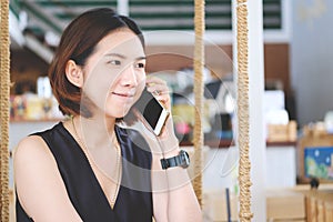 Asian girl listening to a call on her mobile phone, Young beautiful thai woman talking with smiley face in modern cafe