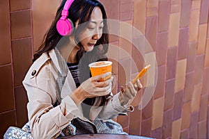 Asian girl listening to music while working, cheerful asian woman drinking coffee outdoors using modern smartphone device