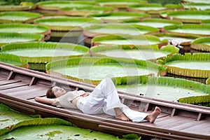 Asian Girl is lying down on the new vintage wood boat on the Lily Lotus Leaf pond at outdoor field