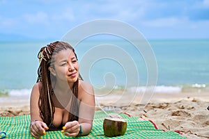 Asian girl lying on the ocean shore smiling next to a coconut