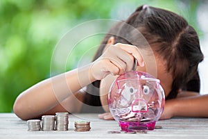 Asian girl making stacks of coins and putting money into piggy bank