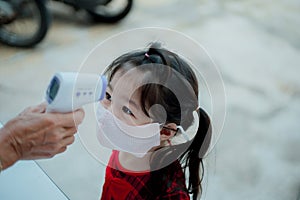 Asian girl measuring body temperature and wearing a face mask