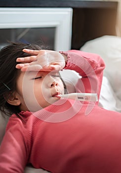 Asian girl measuring temperature herself and hand on forehead with digital thermometer in her mouth on bed at morning time, Sick