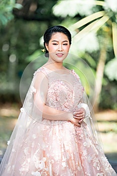 Asian girl in an old rose pink color knee length fluffy dress with high heel slingback shoes and ceremonial thread on her wrist.