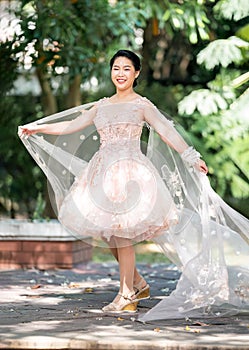 Asian girl in an old rose pink color knee length fluffy dress with high heel slingback shoes and ceremonial thread on her wrist.