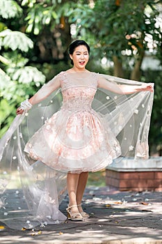 Asian girl in an old rose pink color knee length fluffy dress with high heel slingback shoes and ceremonial thread on her wrist.