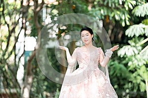 Asian girl in an old rose pink color knee length fluffy dress with high heel slingback shoes and ceremonial thread on her wrist.