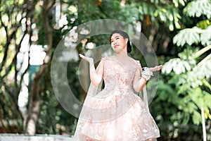 Asian girl in an old rose pink color knee length fluffy dress with high heel slingback shoes and ceremonial thread on her wrist.