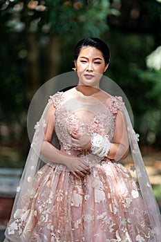 Asian girl in an old rose pink color knee length fluffy dress with high heel slingback shoes and ceremonial thread on her wrist.