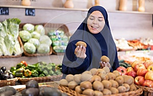 Asian girl in paranja choosing kiwi in grocery