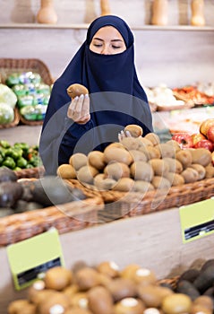 Asian girl in paranja choosing kiwi in grocery