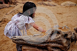 An Asian girl playing in a sandbox with a modeled dinosaur fossil