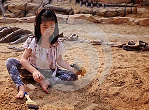 An Asian girl playing in a sandbox with a modeled dinosaur fossil photo