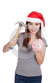 Asian girl with red santa hat hold hammer and pink piggy bank