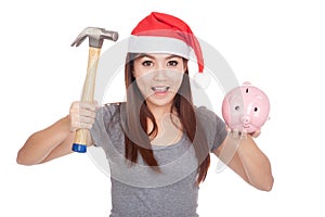 Asian girl with red santa hat hold hammer and pink piggy bank