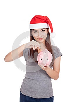 Asian girl with red santa hat put a coin to pink piggy bank