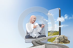 Asian girl in a scarf sitting on a suitcase with a hill view on the mobile phone screen
