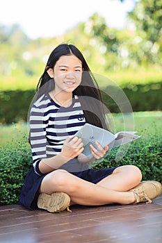 asian girl and school book in hand toothy smiling face with happiness emotion in green park