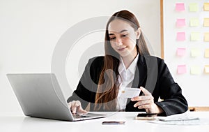 Asian girl shopping online holding credit and using laptop enter their card number in the mobile phone app to purchase and payment