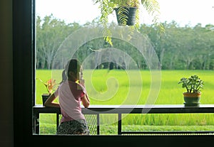 An Asian girl sits on a chair on the balcony, looking at the fields