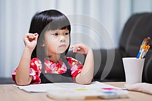Asian girl sits and thinks, imagining the topic of art that will be done today.