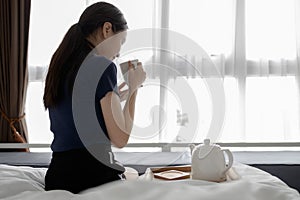 Asian girl sitting on bed drinking hot beverage in the morning,female hold the cup of herbal tea,inhales the smell and smiling