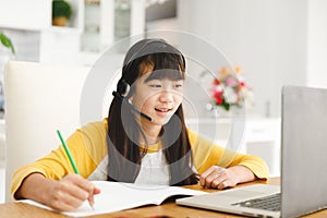 Asian girl sitting at table and using laptop during online lessons