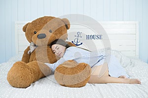 Asian girl sleeping on the bed with a big brown teddy bear.