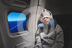 girl sleeping in her seat on the plane near the window in a mask and with a pillow to sleep. The concept of travel with