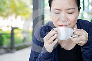Asian girl smelling and enjoying cup of hot coffee at the outside of cafe