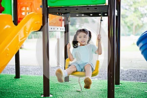 Asian girl smile play swing on school or kindergarten yard or playground. Healthy summer activity for children. Little asian girl