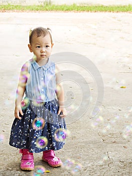 Asian girl standing behind blowing bubbles. Funny activity. Natural acting. Garden view.