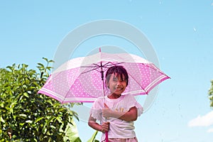 Asian girl standing with an umbrella with joyfulness while it is raining and sunny during the day.
