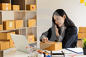 Asian girl startup Small sme business owners work with laptop computers and smartphones at work. with parcel paper boxes for deliv