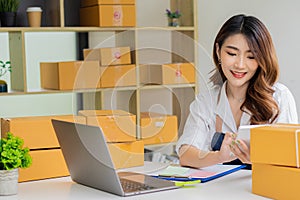 Asian girl startup Small sme business owners work with laptop computers and smartphones at work. with parcel paper boxes for deliv