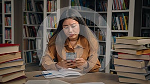 Asian girl student sitting in library write doing homework frustrated young woman getting notification on mobile phone photo