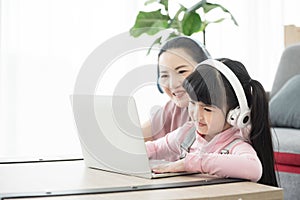 Asian girl studying with laptop and headset ,correspondence course with social distancing, mother sit beside and teach together