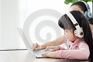 Asian girl studying with laptop and headset ,correspondence course with social distancing, mother sit beside and teach together