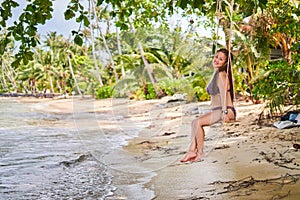 Asian girl swinging on a swing on the bay - palm trees, blurred background