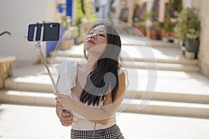 Asian girl taking self portrait on the street - young happy and attractive Asian Japanese woman visiting Seville in Spain taking