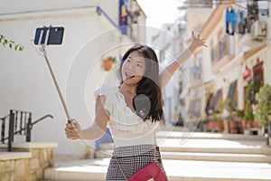 Asian girl taking self portrait on the street - young happy and attractive Asian Japanese woman visiting Seville in Spain taking