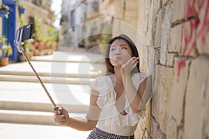 Asian girl taking self portrait on the street - young happy and attractive Asian Japanese woman visiting Seville in Spain taking