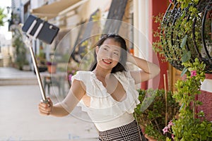Asian girl taking self portrait on the street - young happy and attractive Asian Japanese woman visiting Seville in Spain taking