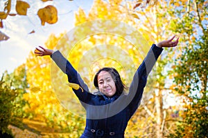 Asian Girl Tossing Yellow Autumn Leaves in the Air in the Park