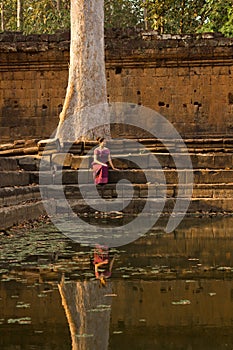 Asian Girl in Traditional Dress Sits by a Tree and Pool of Water in Angkor