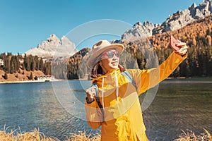 Asian girl travel blogger taking selfie photos at majestic mountain lake and high peaks at the background
